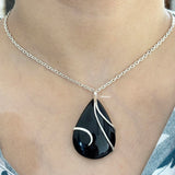 Black teardrop pendant on a silver chain necklace worn by a person.