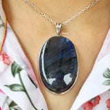 Necklace with a large Labradorite stone pendant on a person wearing a floral dress.